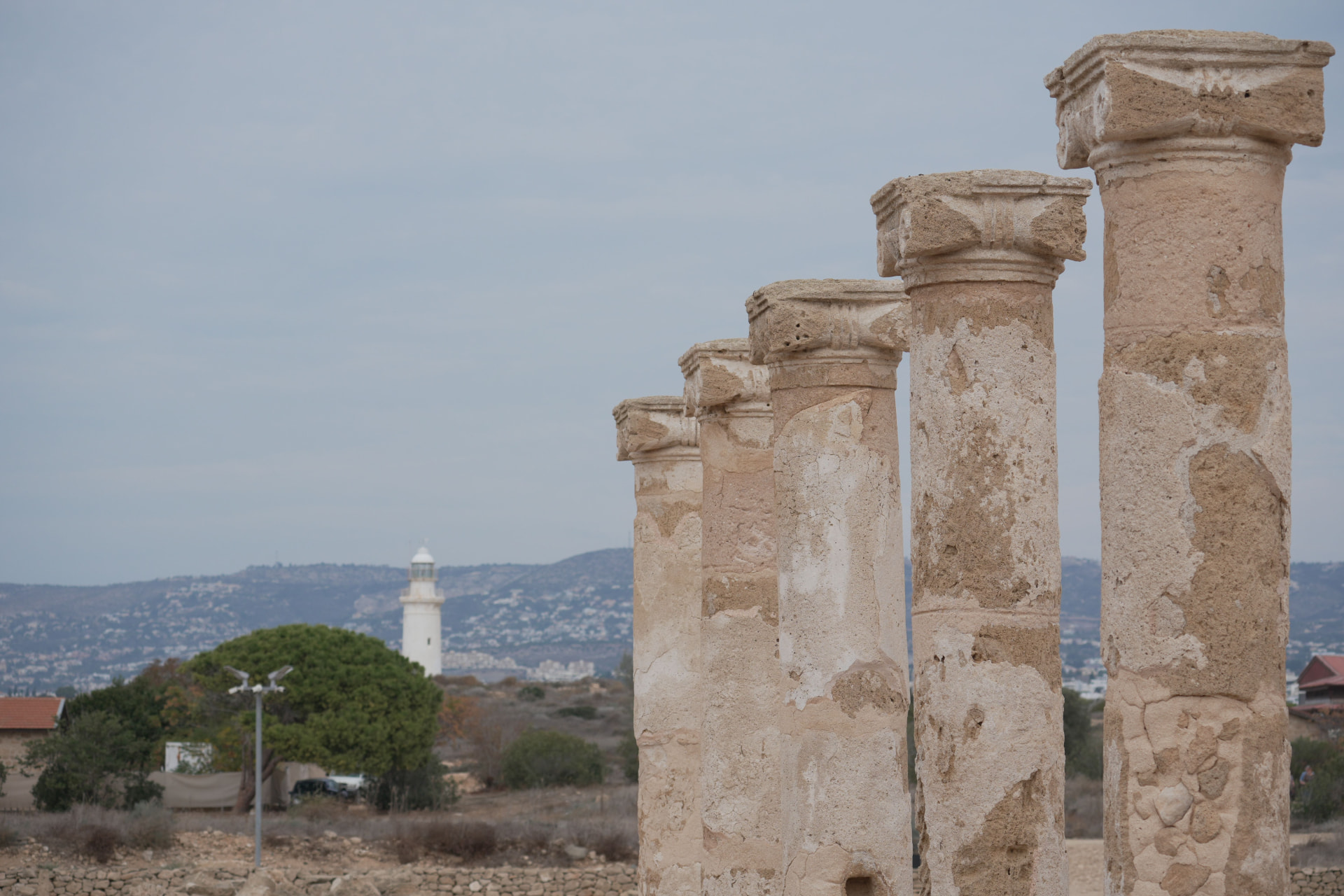 Row of ancient stone columns at the Paphos archaeological park with the lighthouse behind